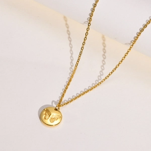 Macro shot of gold stainless steel necklace featuring a circular pendant with butterfly relief