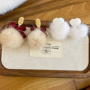 Close-up of heart and bow faux fur earrings on a wooden display tray for winter