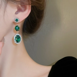 Detailed close-up of emerald green zircon drop earrings with gold finish and clear crystals