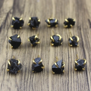 Macro shot of irregular black raw stone earrings with gold claw setting on wood