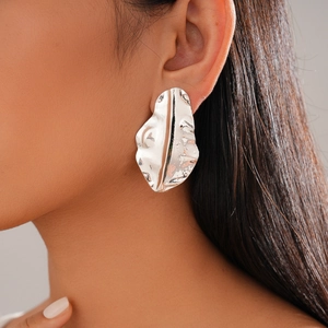 Macro detail of irregular silver-tone leaf earrings with hammered metal texture on model