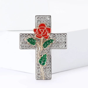 Macro detail of rhinestone cross brooch with red enamel rose on polished silver alloy
