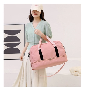 Pink large travel duffel bag with bottom compartment held by model in indoor setting
