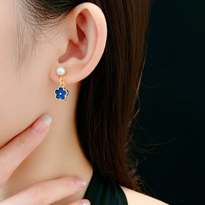 Close-up of elegant blue flower earrings with pearls worn by a model on dark background