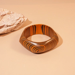 Macro shot of geometric wooden bangle with orange zebra stripes and rustic stone decor