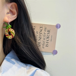 Close-up of handmade beaded Christmas wreath earrings worn by a model in a cozy setting