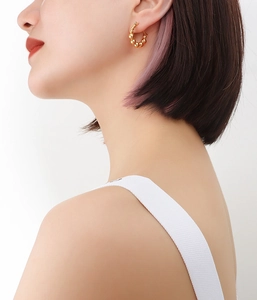 Close-up of a model wearing golden beaded hoop earrings crafted in 18k gold plated steel