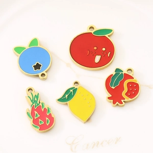 Detailed close-up of fruit-shaped enamel charms on a white ceramic plate tray