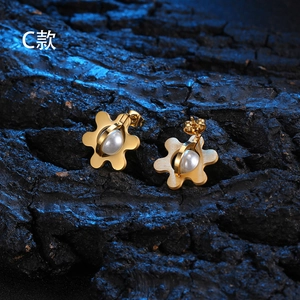 Detail shot of golden floral titanium steel earrings with pearl inlay on a dark stone base