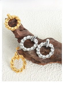 Detail of twisted hoop earrings in gold and silver finish on a natural wood stand
