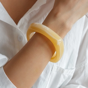 Macro view of yellow marble textured resin bracelet on wrist with elegant white shirt