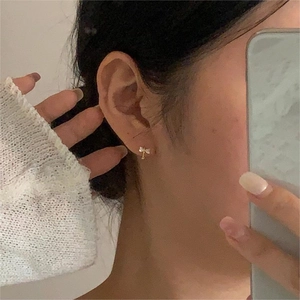 Close-up of a model wearing minimalist gold bow earrings with white shell inlay accents