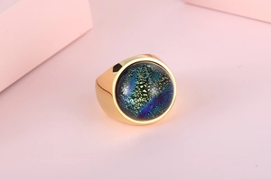 Close-up of golden stainless steel ring with a colorful blue-green textured glass dome