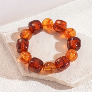 Close-up of amber acrylic beaded bracelet with textured square and round beads on white stone