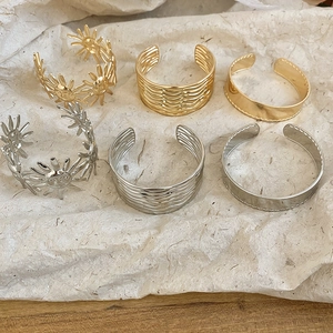 Detailansicht von sechs strukturierten Armreifen in Gold und Silber auf Papierhintergrund.