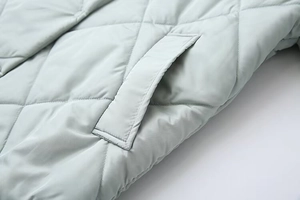 Detailed close-up of diamond quilted stitching on light mint green hooded jacket