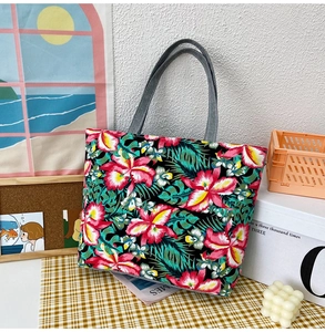 Detail of floral canvas tote bag featuring vibrant tropical leaves and sturdy grey handles