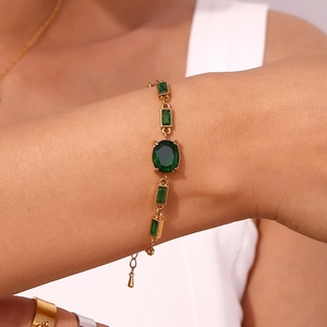 Détail d'un bracelet en acier doré orné de pierres précieuses vertes ovales porté au poignet
