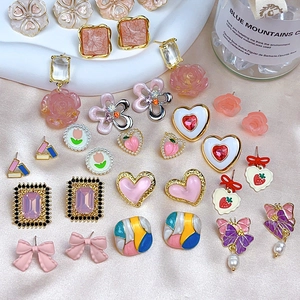 Detailed flat lay of pink heart and floral earrings with pearl accents on satin fabric