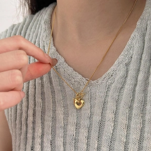 Close-up of a gold heart pendant necklace with a toggle clasp worn on a model