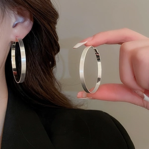 Close-up of model wearing large flat silver hoop earrings with a brushed metallic finish
