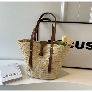 Detail of woven straw tote bag featuring brown leather handles and golden hardware accents