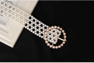 Close-up of elegant white pearl belt featuring a decorative golden round buckle