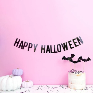 Black Happy Halloween paper banner hanging on a pink wall with festive party decorations