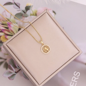 Detailed view of 18K gold scorpion zodiac pendant with sparkling CZ stones on jewelry box