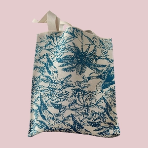 Detail of beige woven tote bag with teal Toile de Jouy pattern and dual carry handles