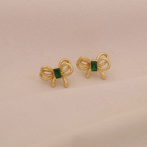 Boucles d'oreilles nœud dorées avec pierre émeraude carrée sur fond rose