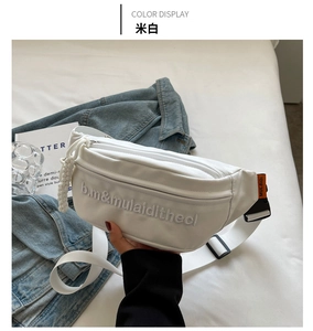 Detail of off-white canvas chest bag featuring textured embroidery and orange buckle strap