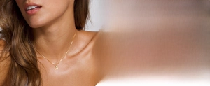 Detail of a minimalist gold initial A pendant necklace on a delicate chain worn by a model
