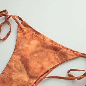 Detailed view of orange tie-dye bikini bottoms with adjustable side-tie strings and texture
