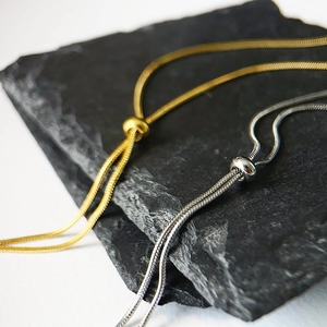 Close-up of adjustable snake chain necklaces in gold and silver finish on a stone surface