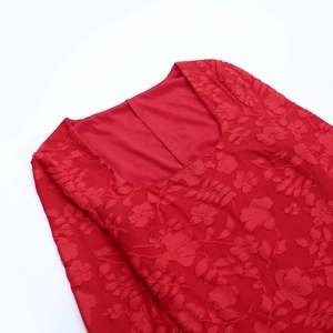Dettaglio di un abito rosso a spalle scoperte con pizzo floreale e trama jacquard