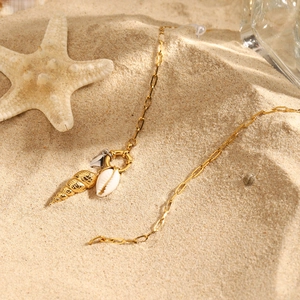 18K gold stainless steel necklace with conch and shell charms on sandy beach background