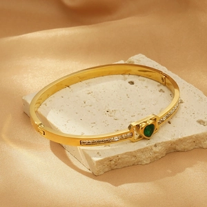 Detailed shot of golden heart bracelet with green gemstone on stone and silk background