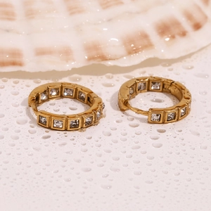 Detail of gold hoop earrings with square zircon crystals on a wet textured surface