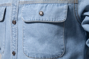 Détail de chemise en jean bleu clair montrant la poche frontale et les coutures jaunes