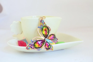 Detailed close-up of a golden butterfly keychain with colorful gemstones on a ceramic cup