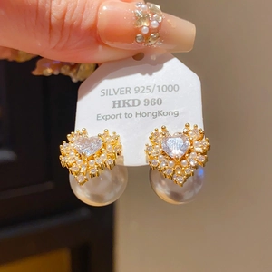 Détail macro de boucles d'oreilles en argent doré avec pierre en cœur et perle blanche