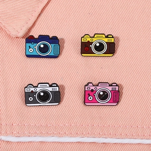Dettaglio macro di quattro spille smaltate a forma di fotocamera su tessuto denim rosa
