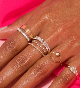 Close-up of gold twist rings and pave band sets worn on a hand over pink velvet