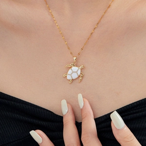 Fashionable gold turtle pendant necklace with white enamel inlay shown on model's neck