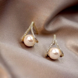 Macro detail of geometric gold earrings with diamonds and round white pearls on silk