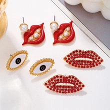 Detail of trendy gold earrings featuring red lips with pearls and devil eye designs