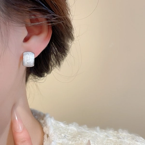 Close-up of minimalist rectangular pearl stud earrings worn by a female model