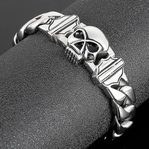 Detail of a polished stainless steel skull charm on a heavy Cuban link biker bracelet