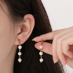 Détail de boucles d'oreilles pendantes dorées avec trois perles d'eau douce alignées